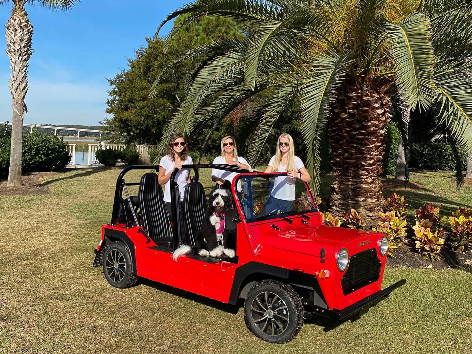 three women and a dog in a red Moke